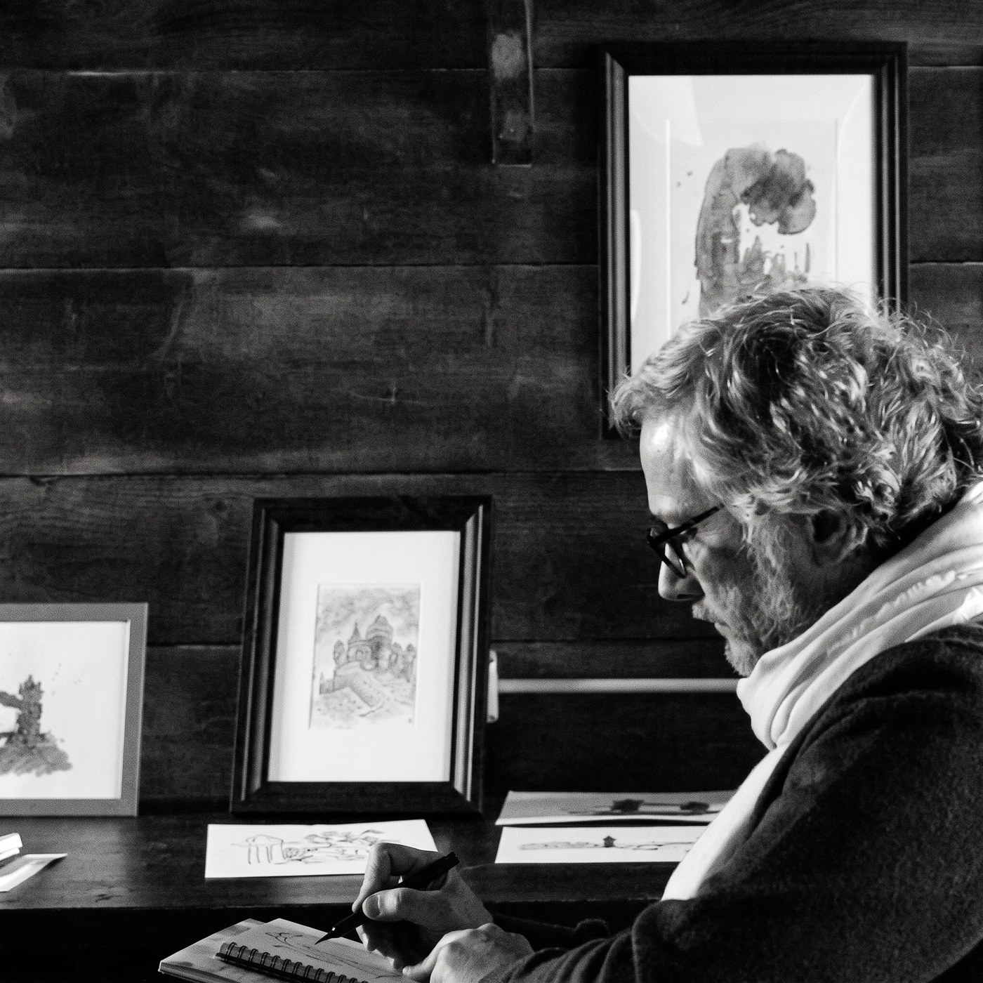 Stefano Mastria drawing in his studio, framed watercolours on the wall behind him