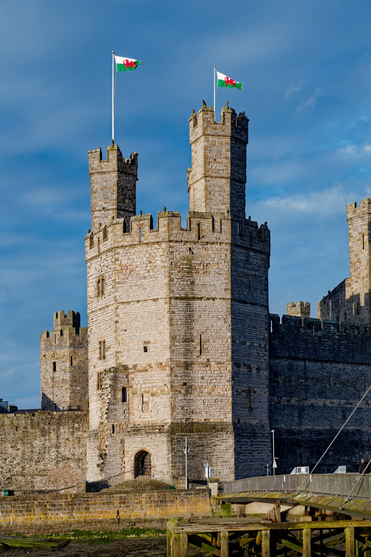 The banded polygonal towers of Caernarfon Castle rising over the water, with Welsh flags flying