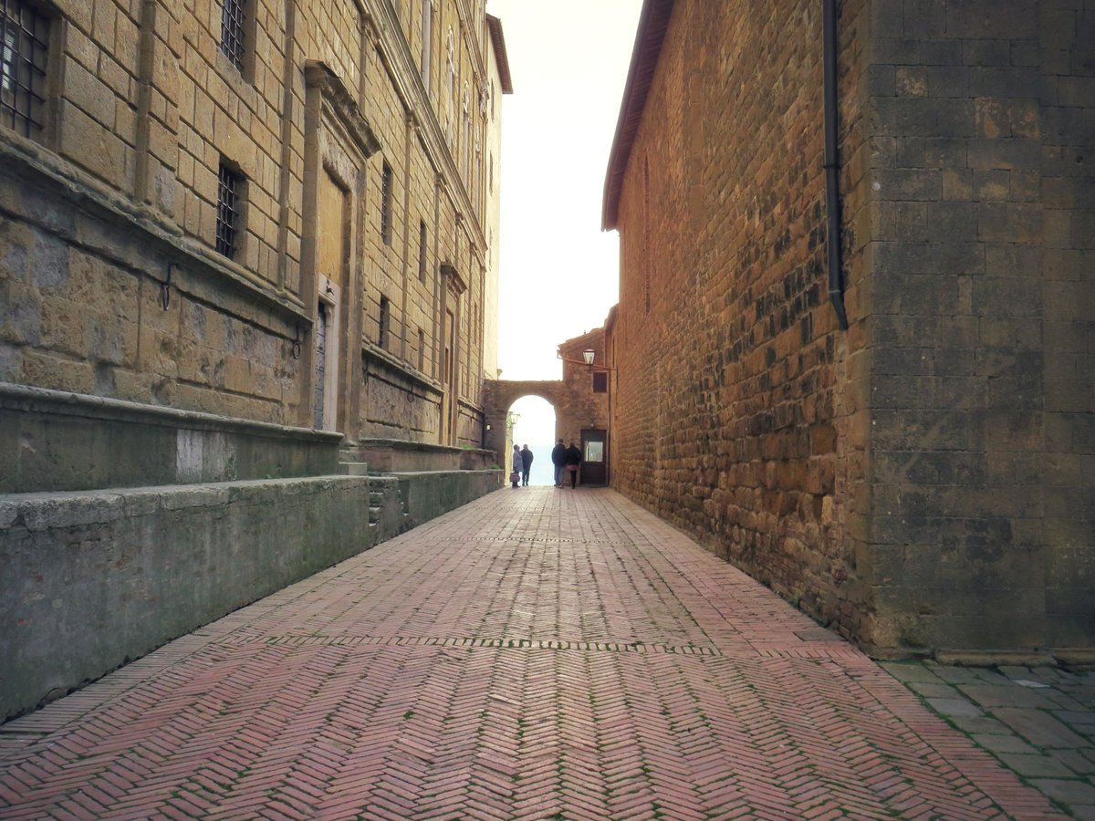 A quiet brick-paved lane in Pienza, Via del Balzello, between warm stone walls