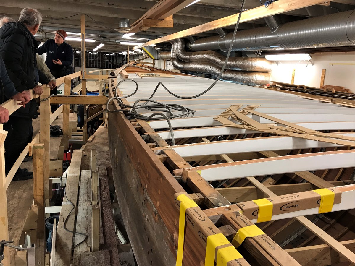 A classic wooden yacht hull under restoration in a boatyard, its oak frames and planking exposed