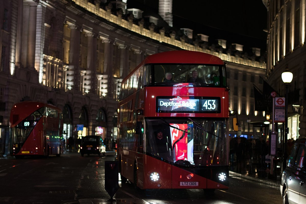 A red double-decker bus on a London street at night