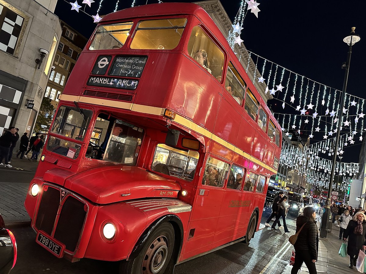 A classic red Routemaster bus on a London street with lights